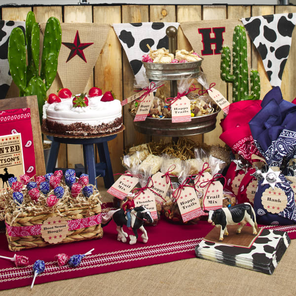 A display set up for a western-themed birthday party. Treats and party favors are accented with Avery labels and tags plus bandannas and cow-print party supplies.