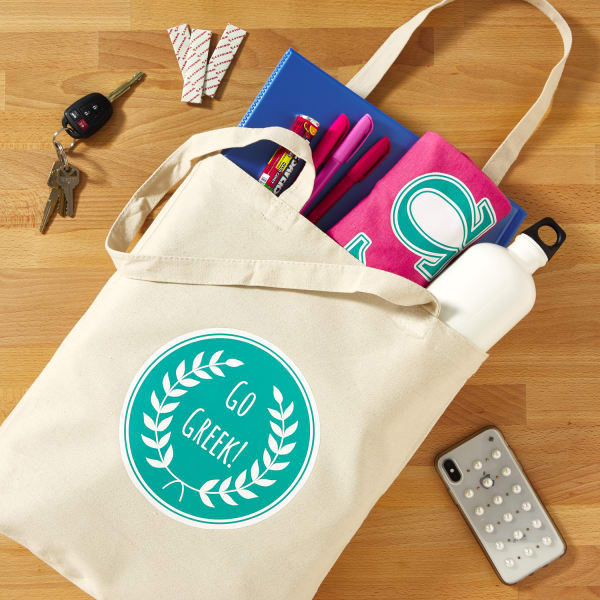 A sorority gift idea that includes a personalized tote filled with swag. The tote is customized with a olive branch design that reads, "Go Greek" using Avery 3271 fabric transfers.