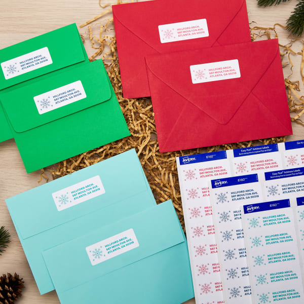 colorful envelopes and custom holiday labels arranged on a pine wood table with packing fill and pine cones for the holidays