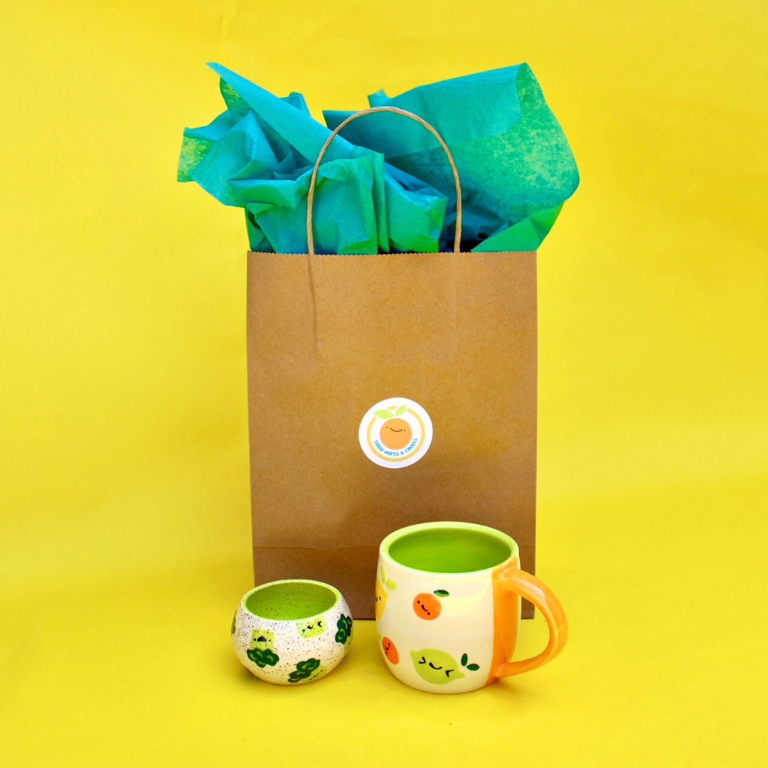 Image of Sakai Harts & Crafts colorful handmade ceramic mug and pot in front of gift bag with customized Avery round label.