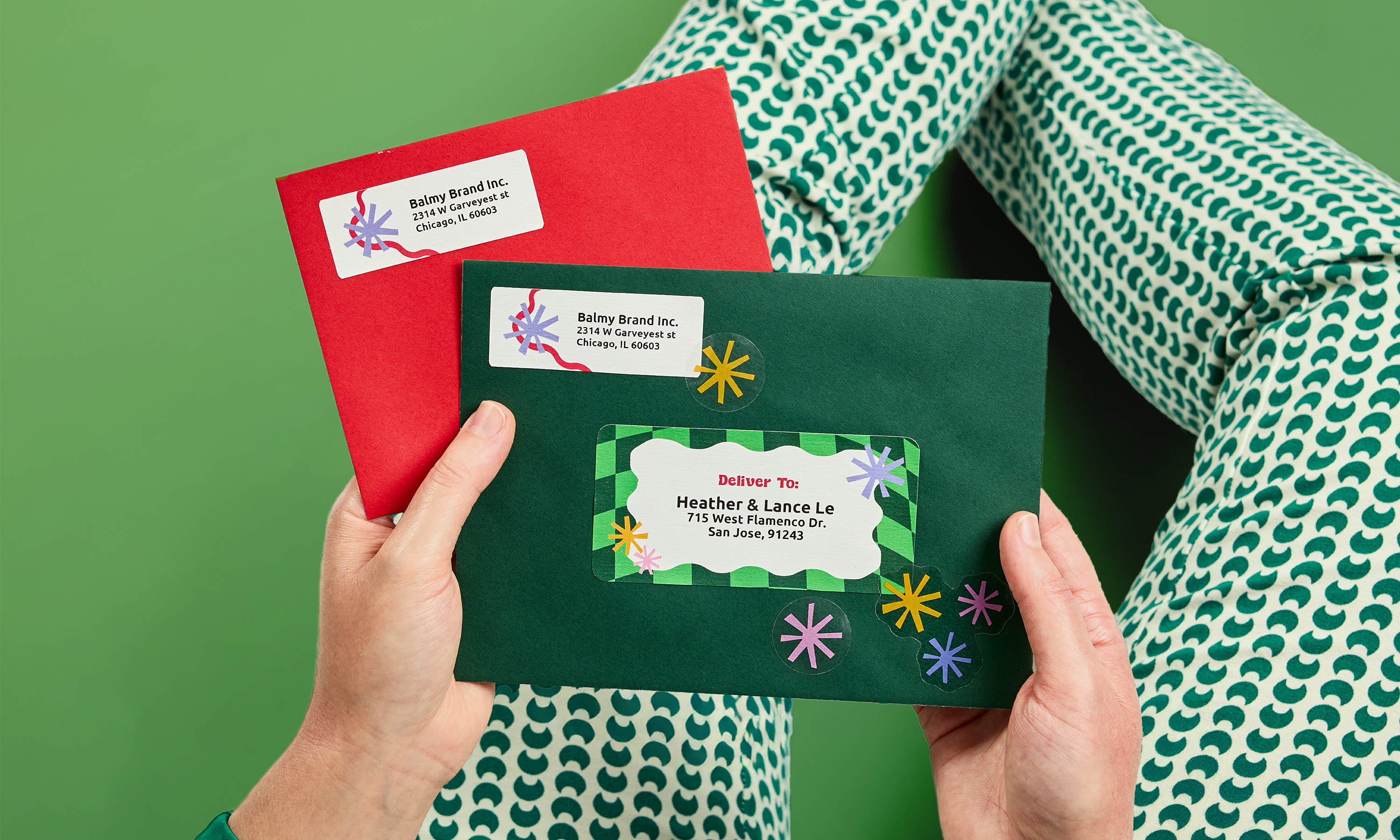 Hands holding a red and a green envelope with decorative Christmas address labels against a green background.