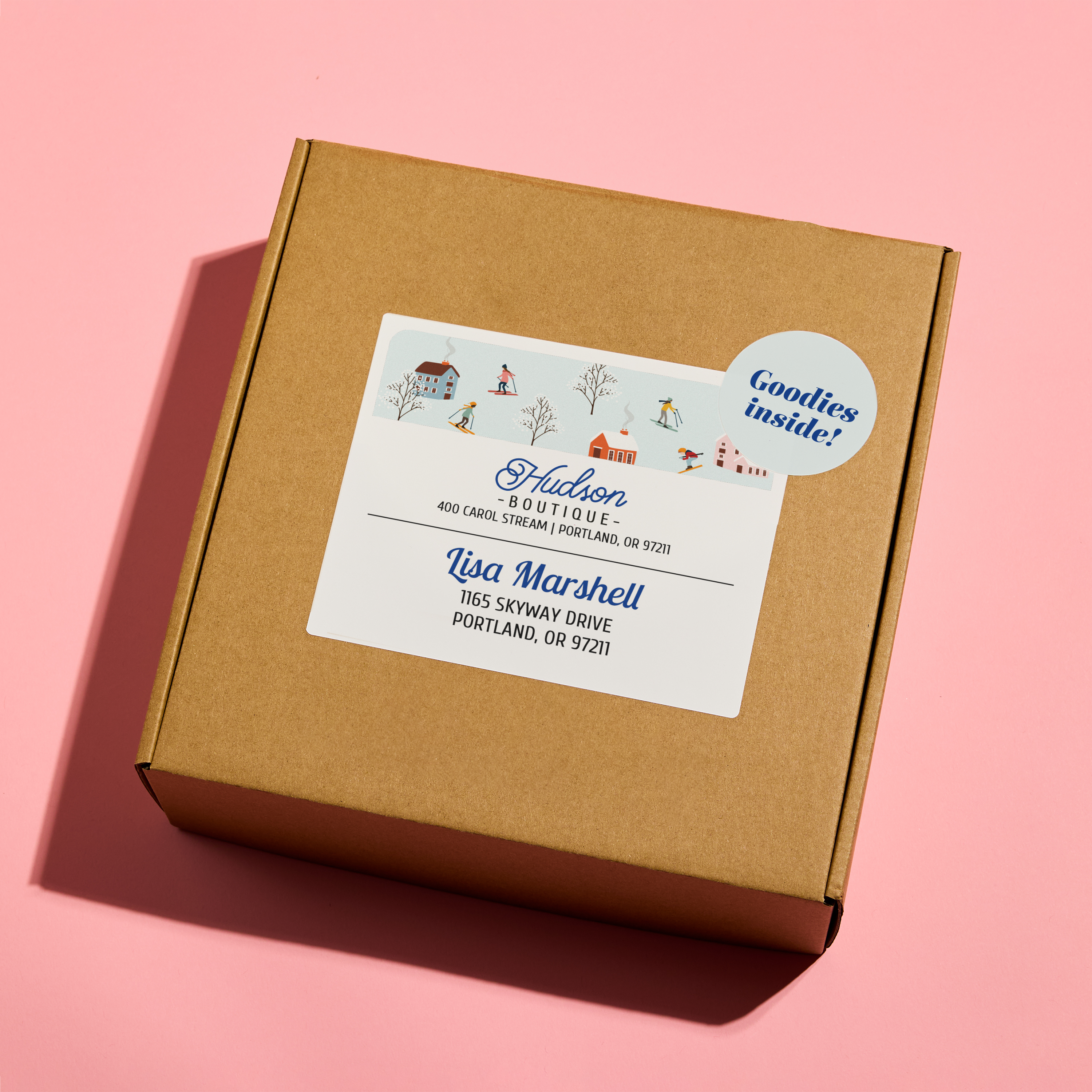 Brown kraft shipping box decorated with a holiday-themed Avery 8164/8154 address label featuring playful seasonal illustrations and “Goodies Inside!” sticker—showing how simple design swaps can create festive packaging.