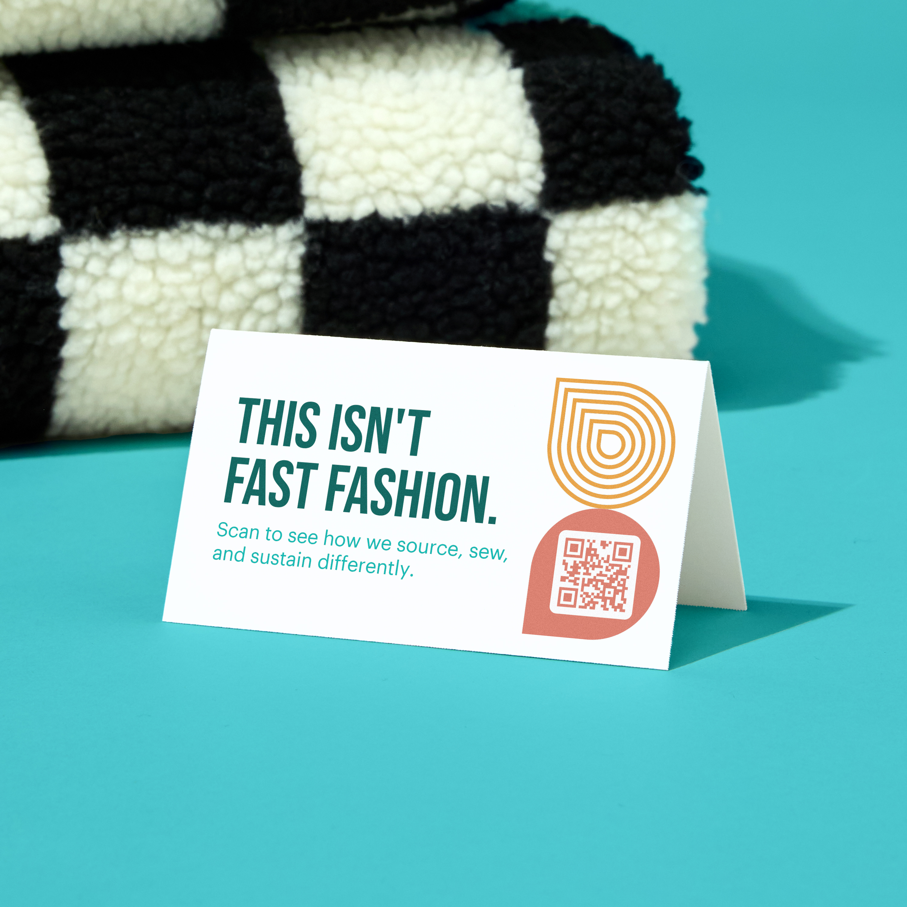 Tent card reading “This isn’t fast fashion” sits in front of a checkered textile, illustrating how small business marketing tools can spotlight mission-driven values.