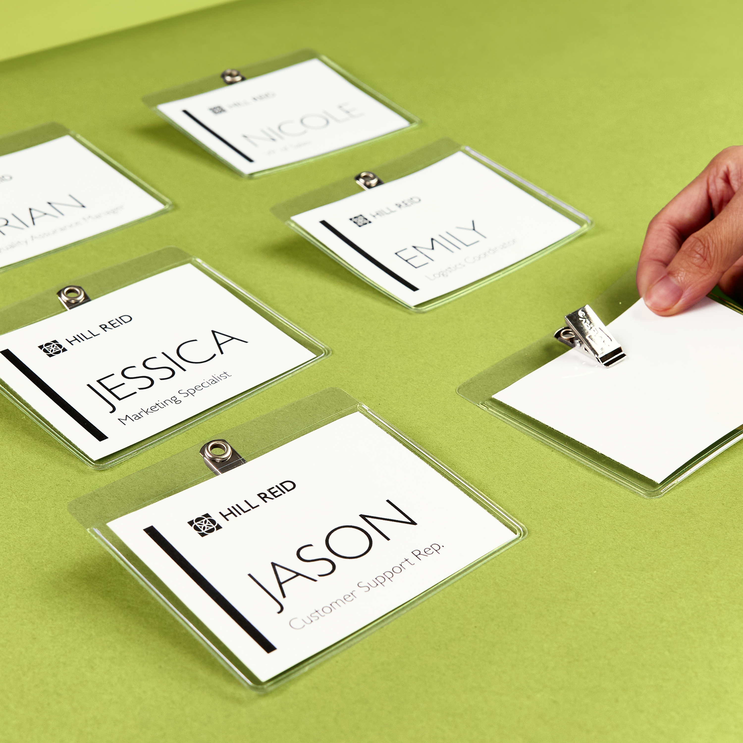 A hand reaches for one of several clip-style name badges labeled with team member names, showing how small business marketing tools support large event staffing and booth roles.