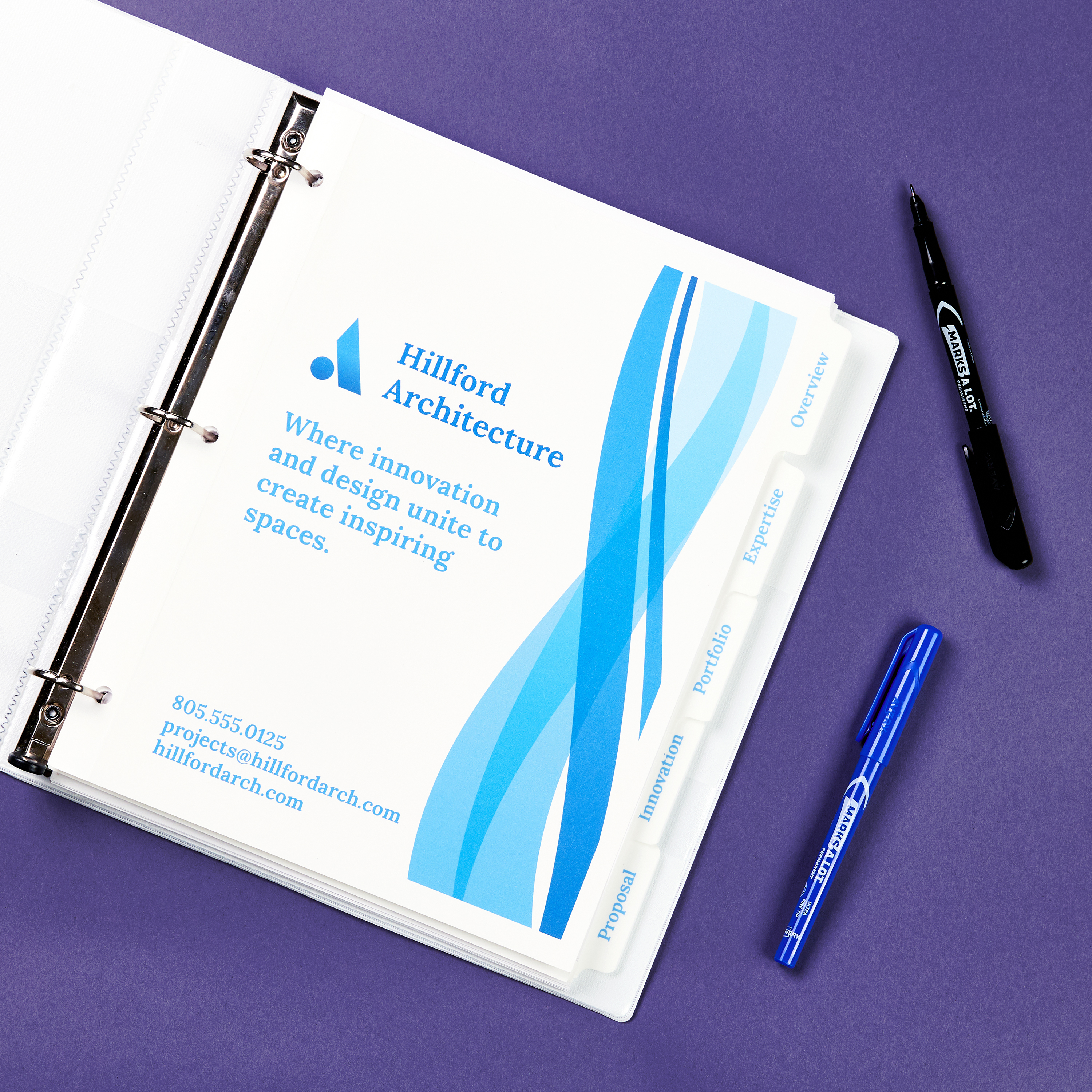 Open binder showing a branded cover page titled “Where Innovation and Elevation Create Inspiring Spaces,” placed on a purple surface with two pens nearby.