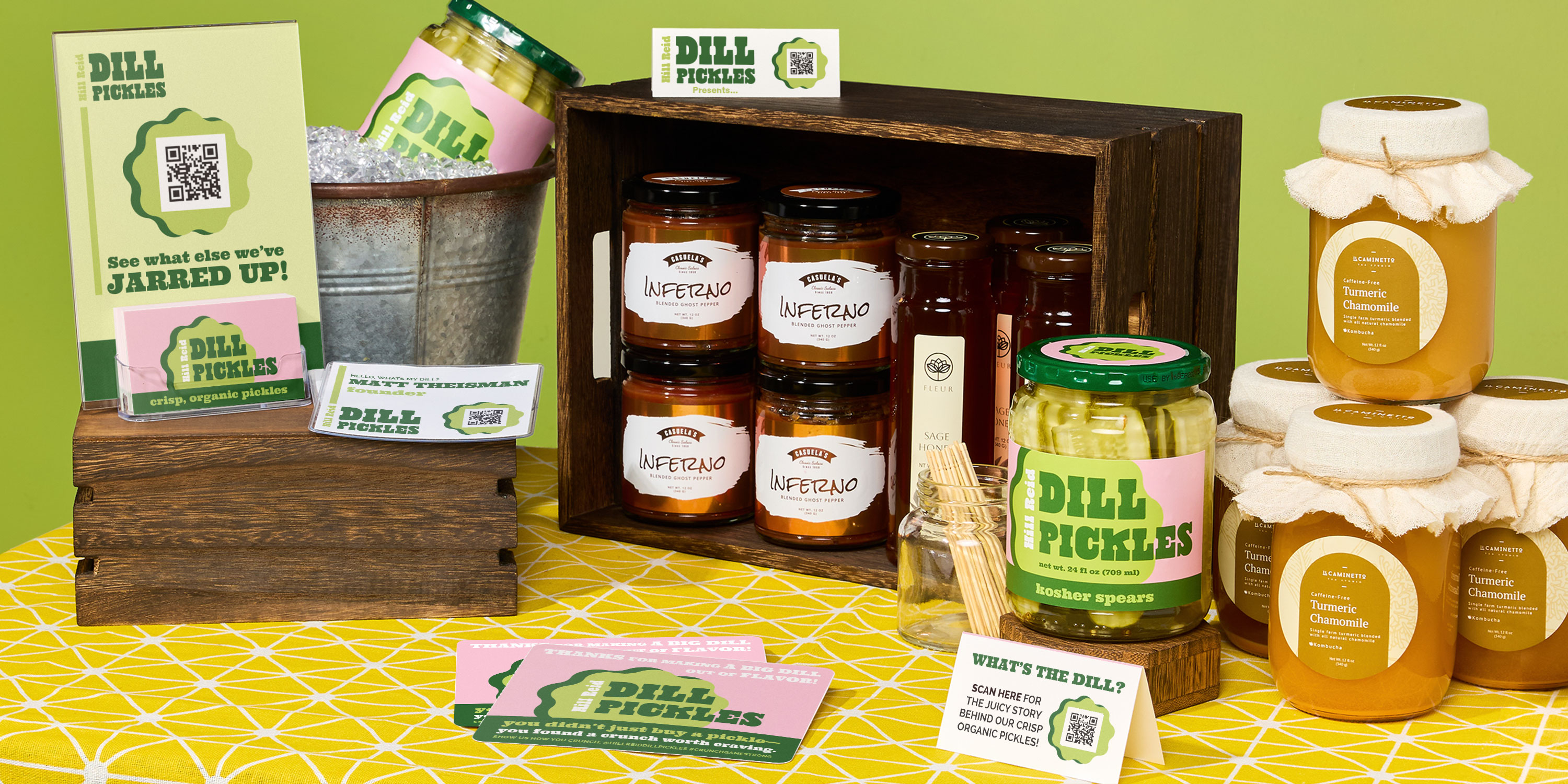 Colorful farmers market table display featuring Hill Reid Dill Pickles, hot sauce, honey, and kombucha, arranged in wooden crates and ice buckets. Includes custom and branded signage with QR codes, business cards, and point-of-sale marketing materials. A creative example of effective farmer market display ideas using cohesive design, jar labels for small businesses, and small-batch products.