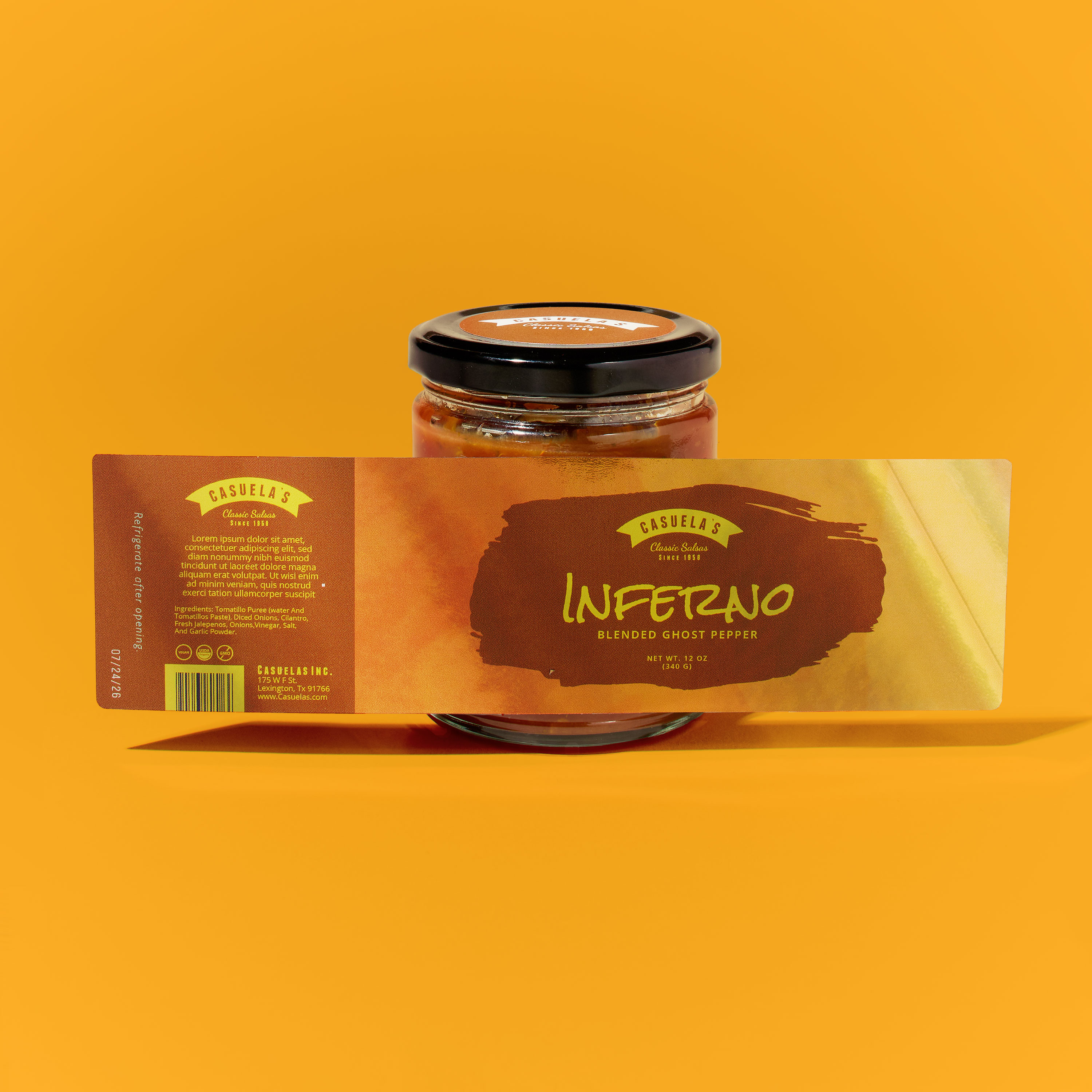 Glass jar of hot sauce placed against a bright orange background. The jar has a black lid with a small round label on top. A large product label is displayed flat in front of the jar to show its full wraparound design. The chrome finish on the label creates a gradient of deep orange to golden yellow. Bold text reads 'Inferno.' The left panel of the label includes smaller product details, icons, and ingredients in yellow text.