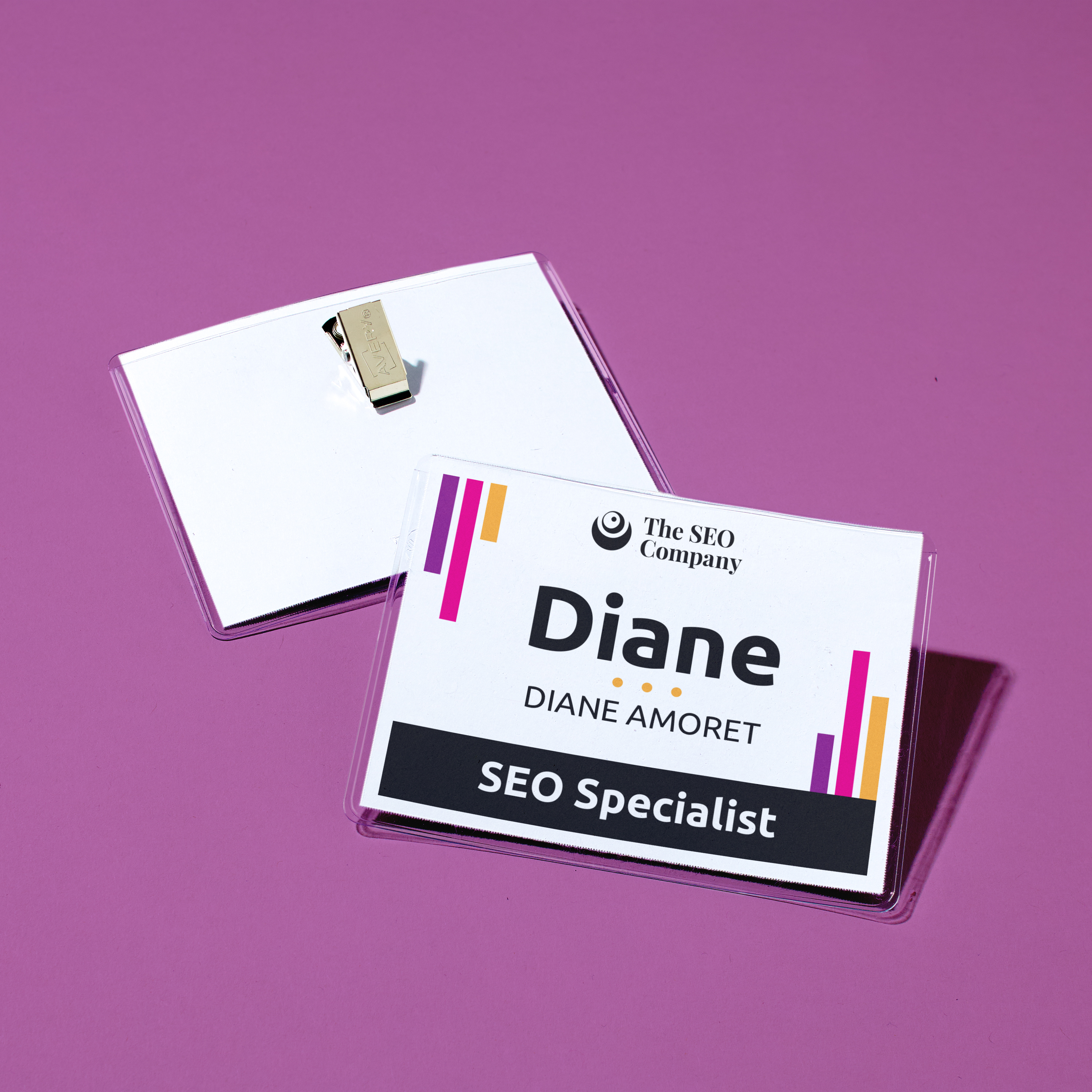 Branded business name tag design for meetings, shown on purple background. Clip-style badge holder displays black text reading “Diane Amoret, SEO Specialist” with colorful orange and magenta accent stripes. The SEO Company logo appears at the top.