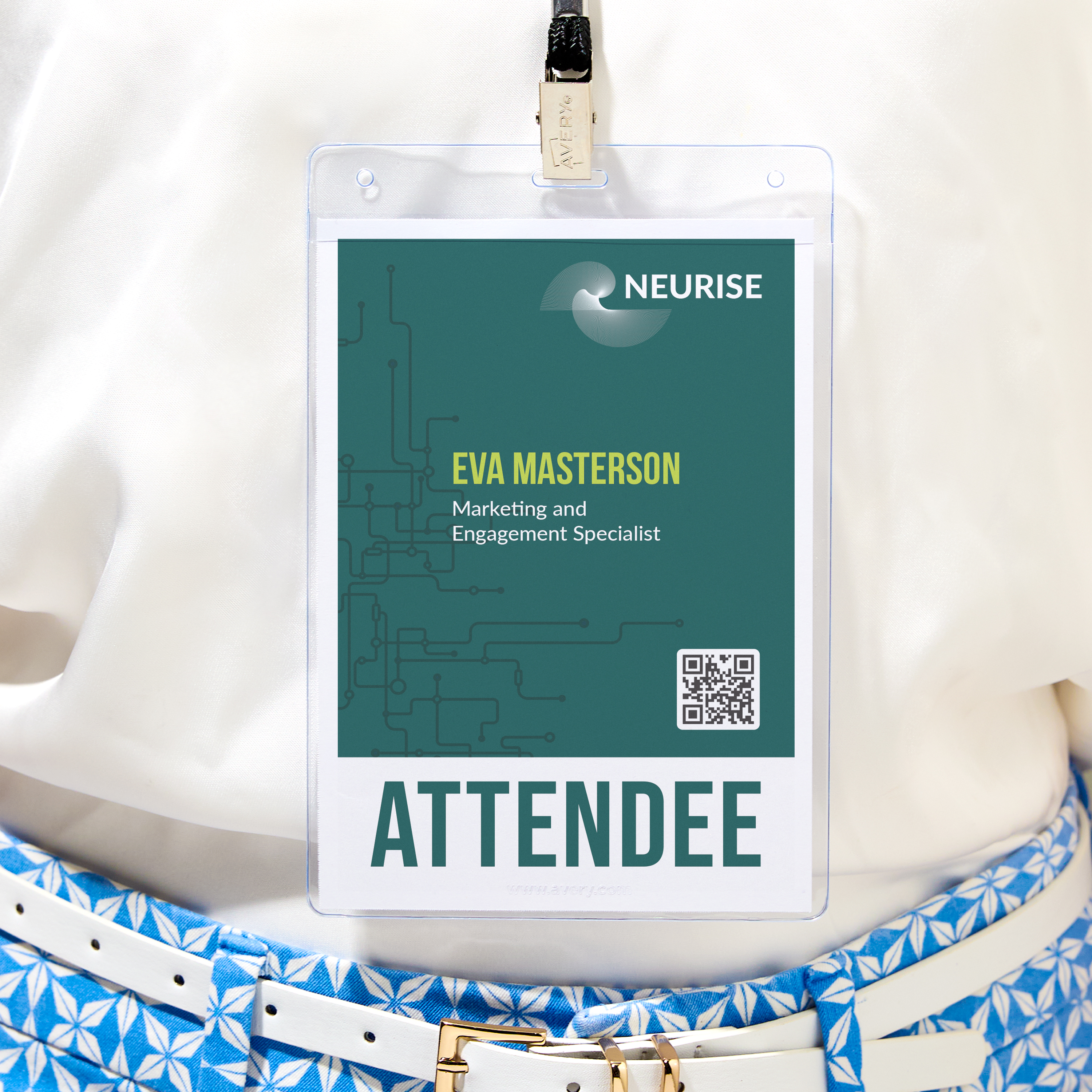 A conference name badge worn on a white blouse with a geometric blue-and-white patterned belt. The badge is enclosed in a clear plastic holder and clipped to a lanyard. It displays the NEURISE logo at the top, followed by the name “Eva Masterson” in bold yellow-green text. Her title, “Marketing and Engagement Specialist,” appears underneath. A QR code is placed in the lower right corner of the badge, and the word “ATTENDEE” is printed in large capital letters at the bottom.