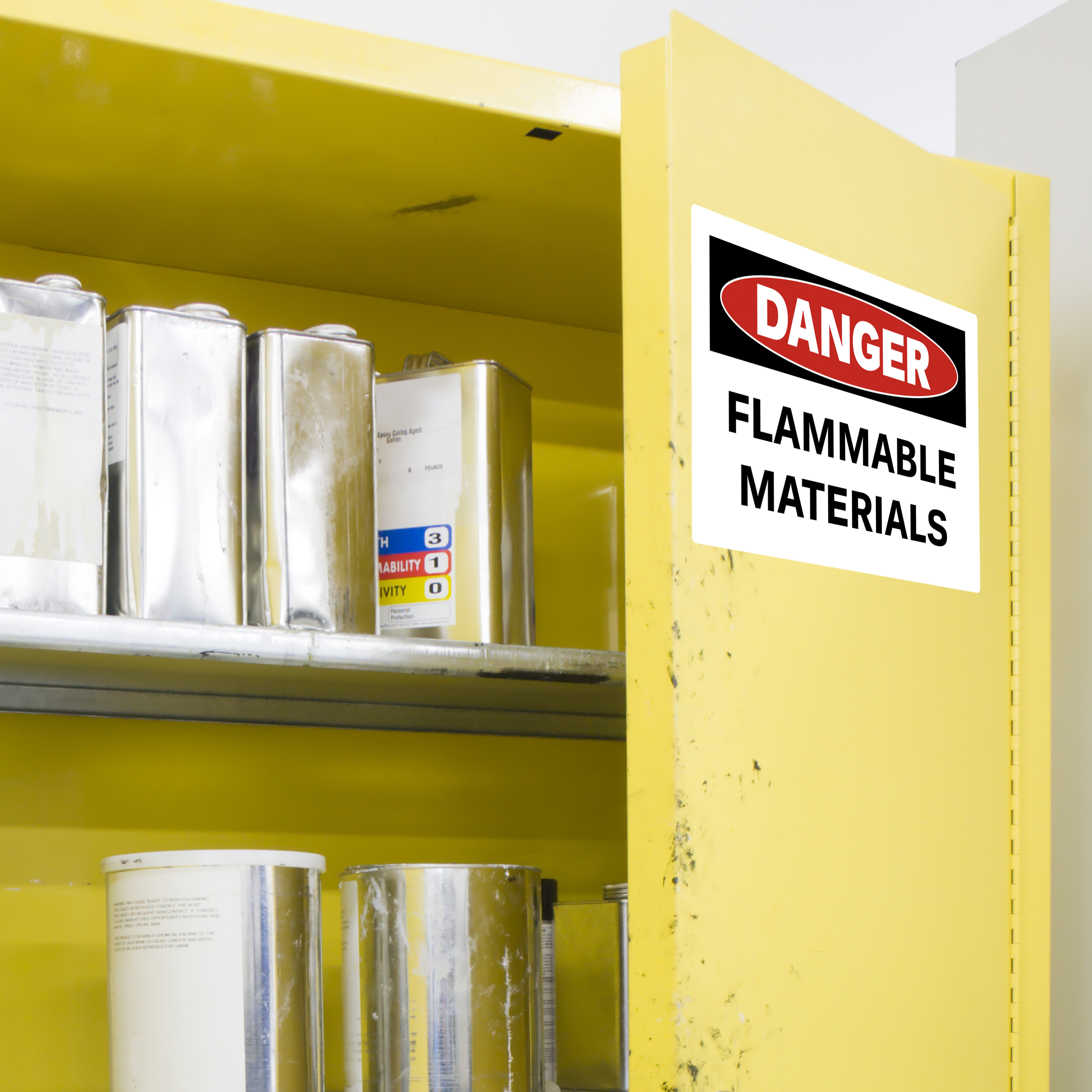 An example of a safety sign for flammable materials with a standard OSHA danger heading. It is applied on a metal cabinet filled with paint supplies and chemicals. The sign is printed on Avery 61552 vinyl sign labels.