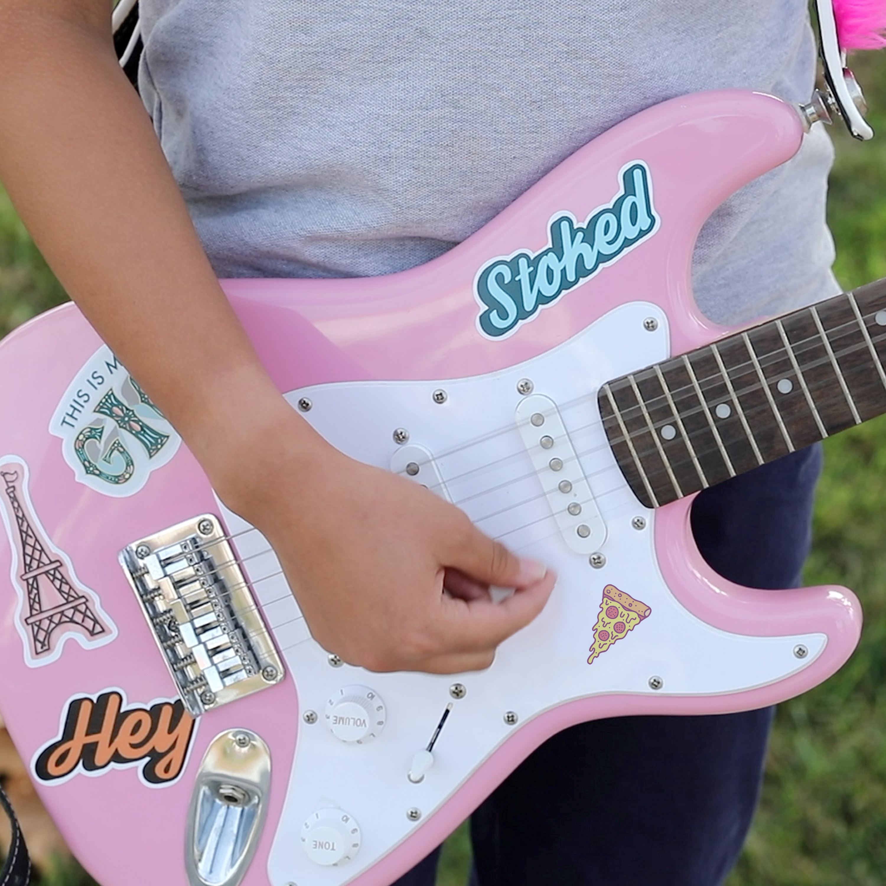 A close up of a tween holding a pink electric guitar. The guitar is decorated with custom stickers made with Avery 61512 decal sheets. 