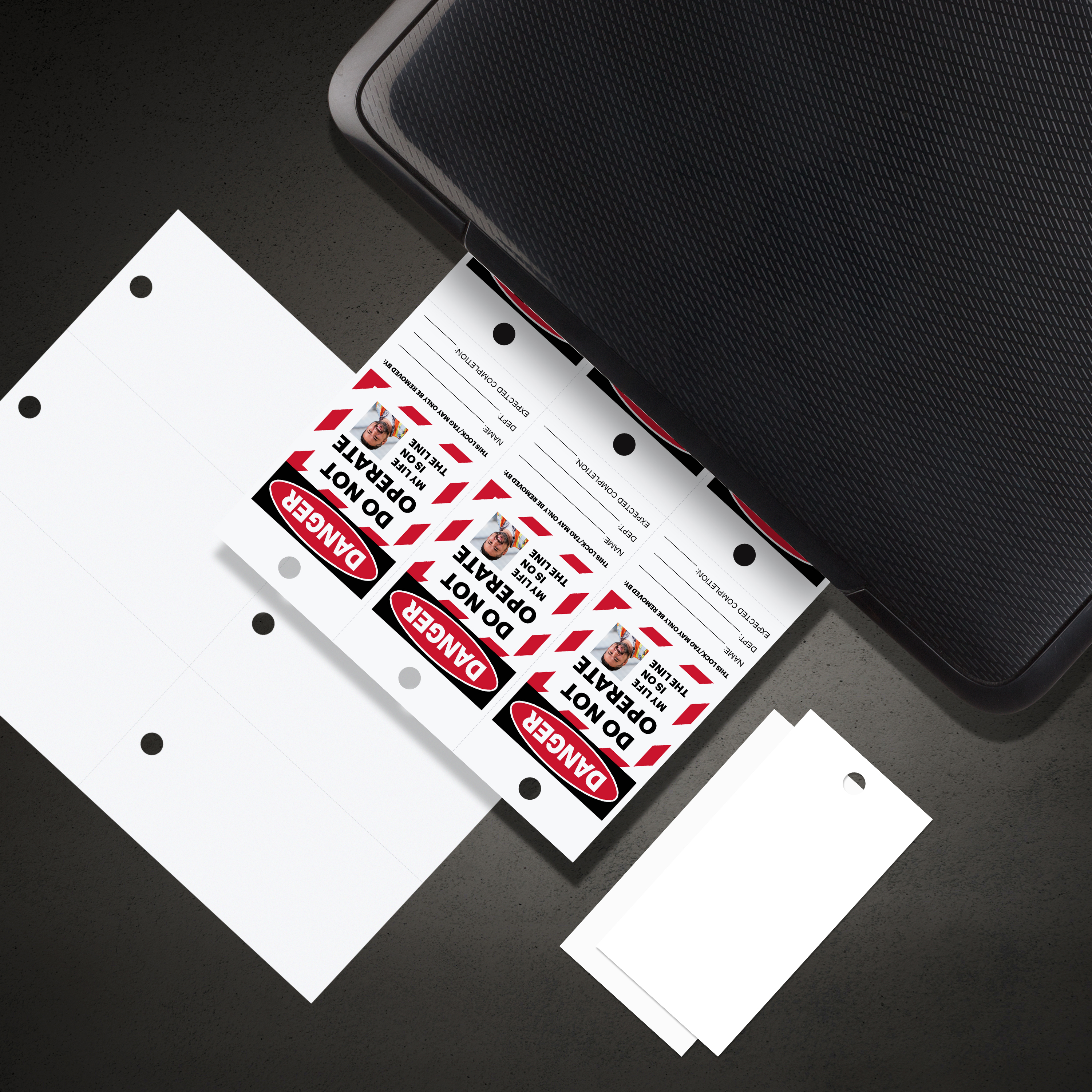 An image showing Avery 62400 safety tags used to make lockout tagout tags. The tags are coming out of a laser printer with the customized LOTO design and there are also blank tags shown before printing. 