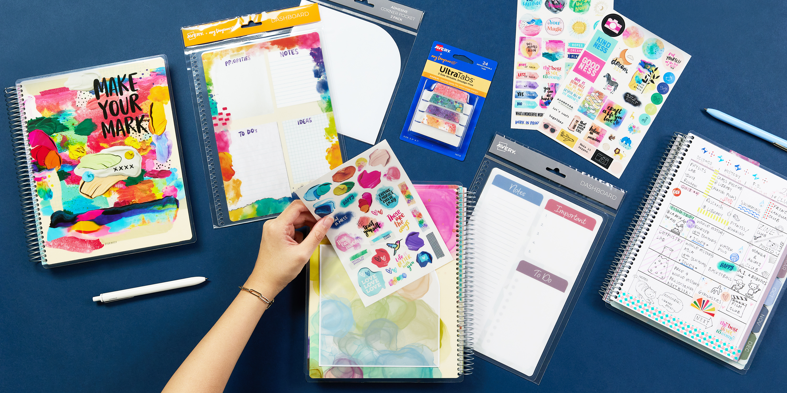 Avery planner accessories are shown spread out on a navy blue background. In addition to Avery academic planners, there are dashboards, planner stickers, Ultra Tabs, and adhesive pockets.