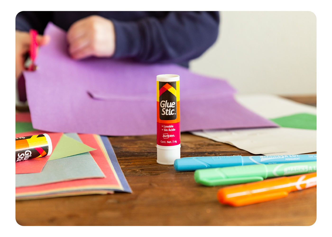 A desktop focusing on an Avery Glue Stic at the center, surrounded by various arts and crafts supplies
